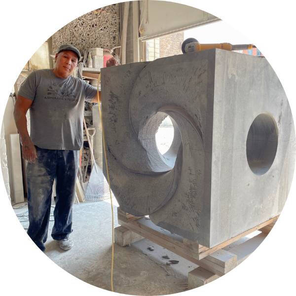 Artist Jason Quigno standing next to one of his large carved stone sculptures.